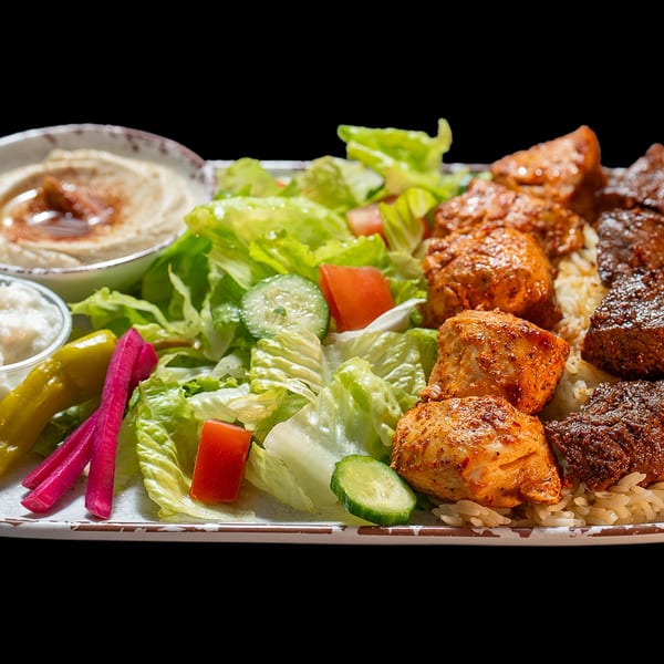 A platter with chicken and beef shawarma, rice, green salad, hummus, and pickles.
