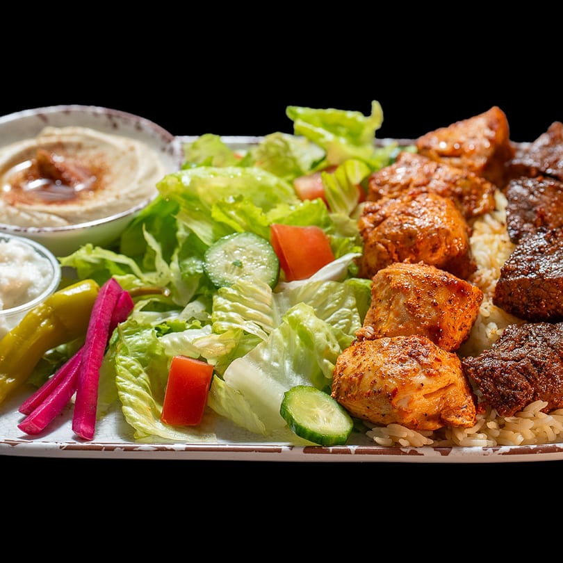A platter with chicken and beef shawarma, rice, green salad, hummus, and pickles.