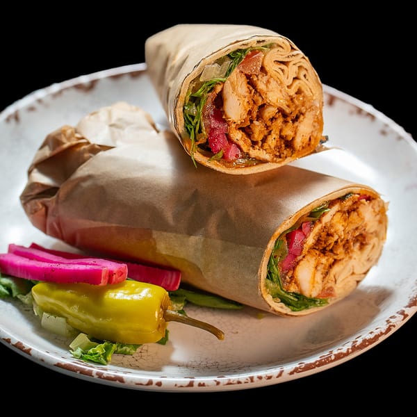 Two chicken shawarma wraps with lettuce, pickles, and a pepper on a white plate.