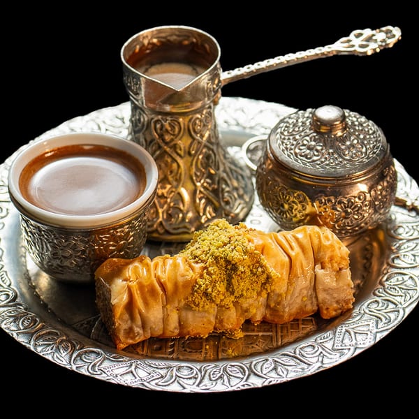 Turkish coffee in ornate silver cups with a sugar bowl and baklava on a silver tray.