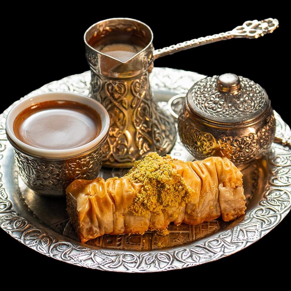 Turkish coffee in ornate silver cups with a sugar bowl and baklava on a silver tray.