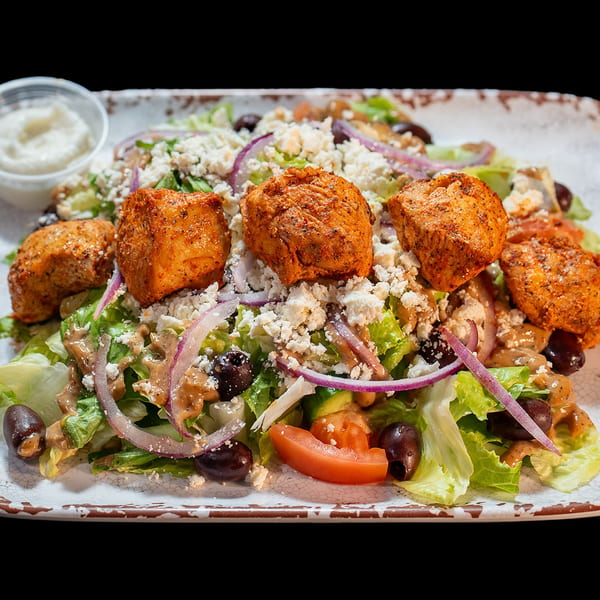 Chicken salad with lettuce, feta, red onions, olives, tomatoes, and a side of dressing.