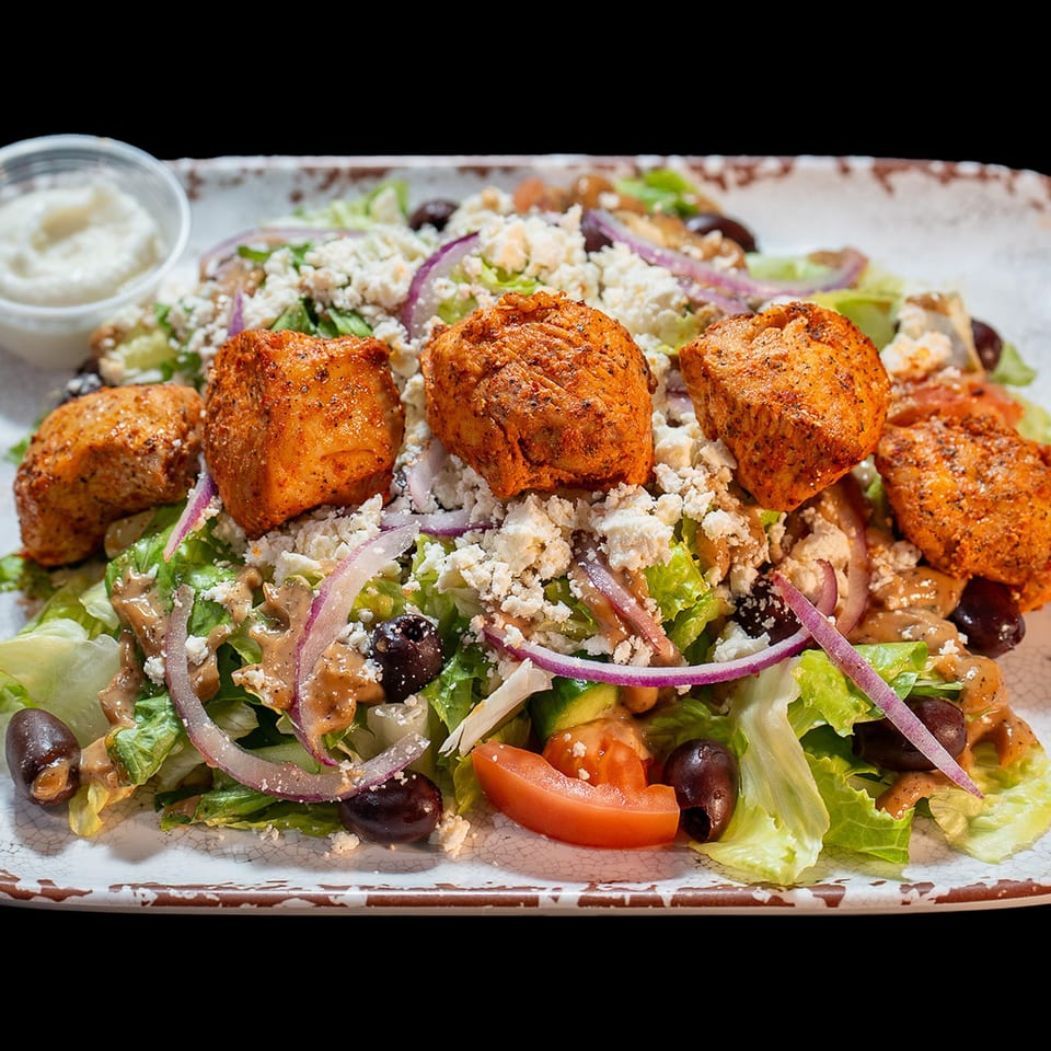 Chicken salad with lettuce, feta, red onions, olives, tomatoes, and a side of dressing.