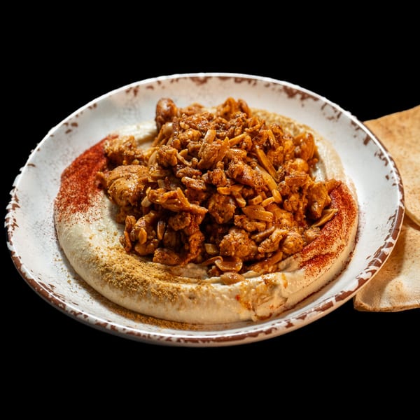 Hummus topped with spiced chicken, sliced almonds, paprika, and cumin, served with pita bread.