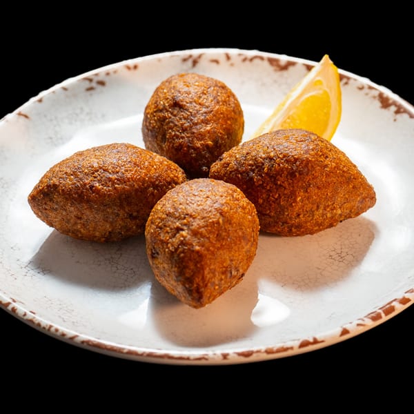 Four golden-brown kibbeh, two round and two oval, with a lemon wedge on a white plate.