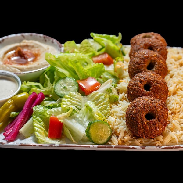 A plate of falafel, rice, salad with tomatoes and cucumbers, hummus, and pickled vegetables.